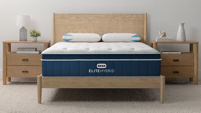 Bear Elite Hybrid mattress styled in modern bedroom with dark wood frame, nightstands, and rug for The Mattress Shop, showcasing product image Bear Elite Hybrid on the page: Best Mattresses 2026 page.