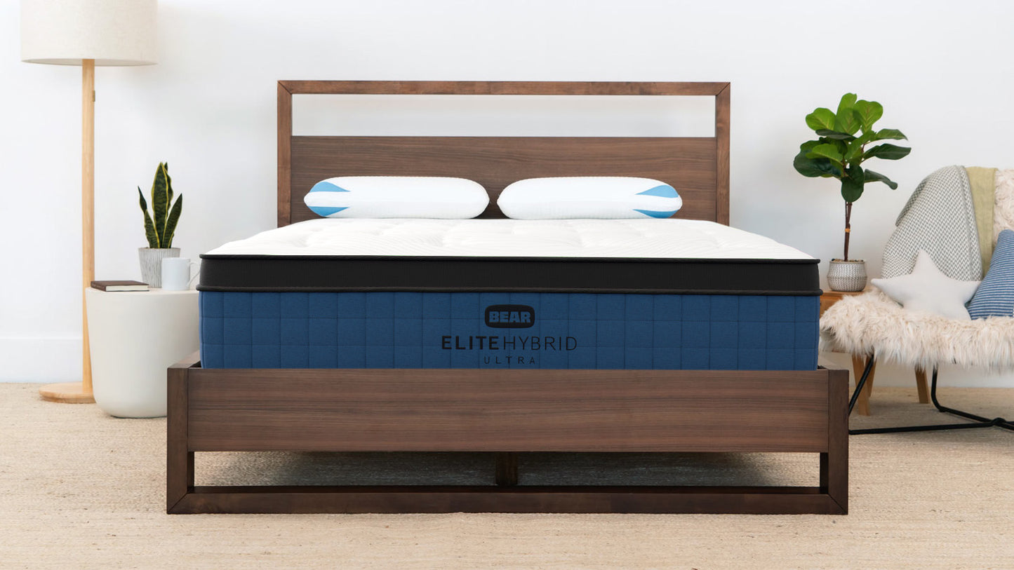 Bear Elite Ultra Hybrid Mattress in navy and white on a walnut bed frame in a bright modern bedroom for The Mattress Shop, showcasing product image for Bear Elite Ultra Hybrid on the product page.