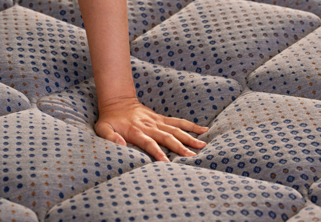 Close-up of Brooklyn Bedding CopperFlex mattress quilted fabric surface with hand pressing into gray patterned ticking showing responsive cushioning for The Mattress Shop, showcasing product image Brooklyn Bedding CopperFlex® on the page: Best Hybrid Mattresses - Quiz Prominent CTA page.