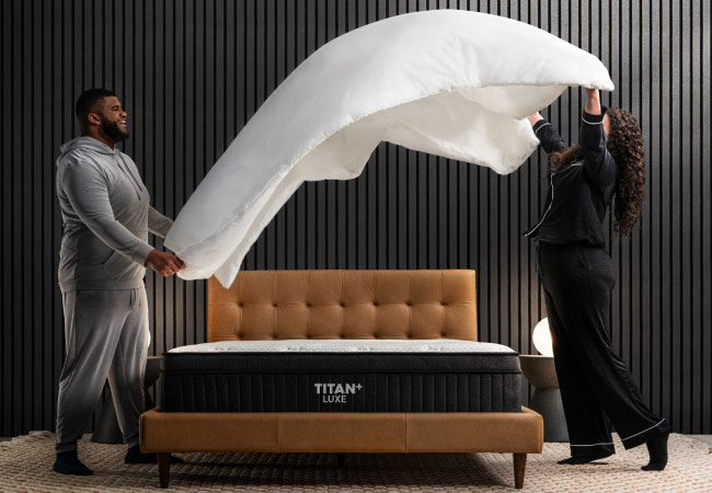 Brooklyn Bedding Titan Plus Luxe mattress, couple tossing comforter over bed in modern bedroom. for The Mattress Shop, showcasing product image Brooklyn Bedding Titan® Plus Luxe on the page: Best Hybrid Mattresses page.