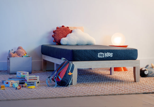 Brooklyn Bedding BB Kids mattress on wood bed frame in colorful children's bedroom with toys and backpack. for The Mattress Shop, showcasing product image for Brooklyn Bedding BB Kids on the product page.