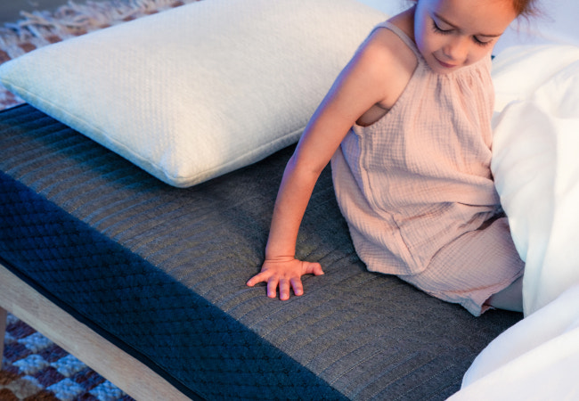 Brooklyn Bedding BB Kids mattress close-up with young child pressing hand into navy blue quilted surface. for The Mattress Shop, showcasing product image Brooklyn Bedding BB Kids on the page: Best Mattresses for Kids page.