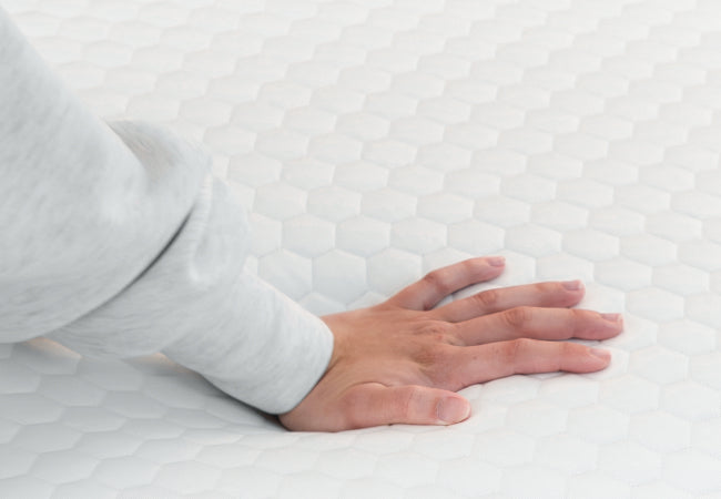 Brooklyn Bedding microcoil mattress topper close-up with hand pressing into honeycomb quilted surface for comfort for The Mattress Shop, showcasing product thumbnail image for Brooklyn Bedding Microcoil Mattress Topper on the product page.