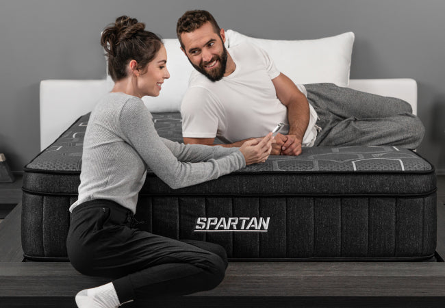 Brooklyn Bedding Spartan mattress, couple relaxing together browsing phone in modern bedroom. for The Mattress Shop, showcasing Monthly financing with Affirm on the page: Contact Us page.
