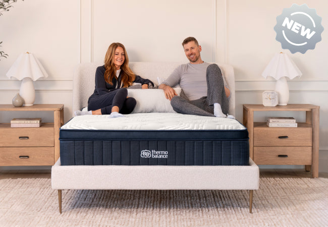 Brooklyn Bedding ThermoBalance LX new mattress, couple sitting together on white pillow top bed for The Mattress Shop, showcasing product thumbnail image for Brooklyn Bedding ThermoBalance LX on the product page.