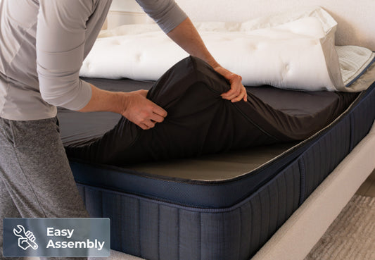 Brooklyn Bedding ThermoBalance LX Elite mattress easy assembly, man attaching pillow top to navy base for The Mattress Shop, showcasing product image for Brooklyn Bedding ThermoBalance LX Elite on the collection page.