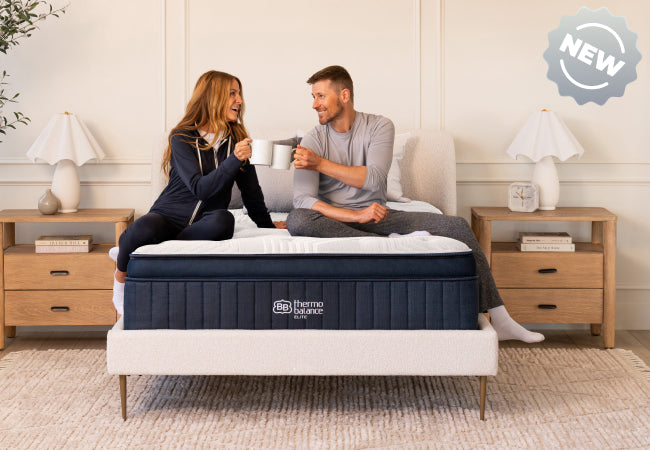 Brooklyn Bedding ThermoBalance LX Elite new mattress, couple sitting on bed toasting mugs together for The Mattress Shop, showcasing product thumbnail image for Brooklyn Bedding ThermoBalance LX Elite on the product page.