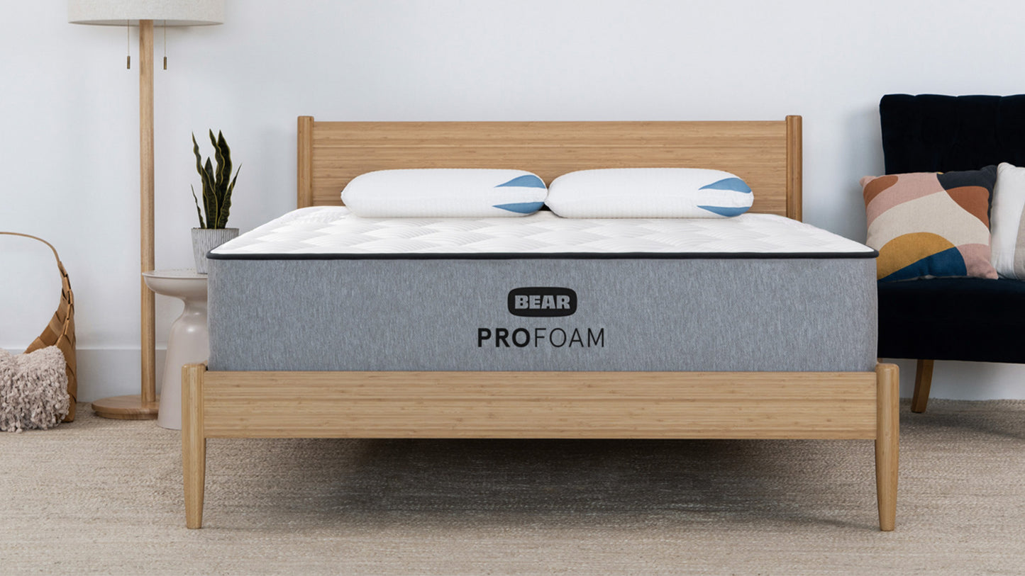 Bear Pro Foam mattress on bamboo bed frame in modern bedroom with floor lamp and navy accent chair for The Mattress Shop, showcasing product image for Bear Pro Foam on the product page.