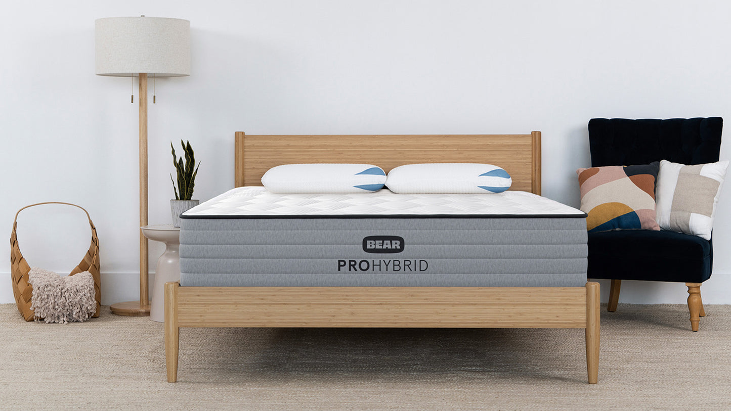 Bear Pro Hybrid Mattress in bright modern bedroom with natural wood bed frame and matching pillows for The Mattress Shop, showcasing product image for Bear Pro Hybrid on the product page.
