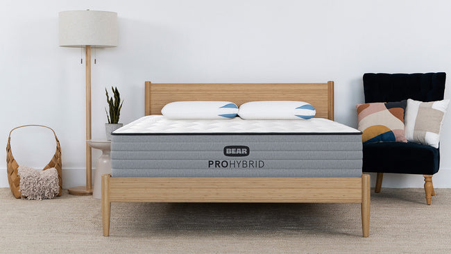 Bear Pro Hybrid Mattress in bright modern bedroom with natural wood bed frame and matching pillows for The Mattress Shop, showcasing product thumbnail image for Bear Pro Hybrid on the product page.