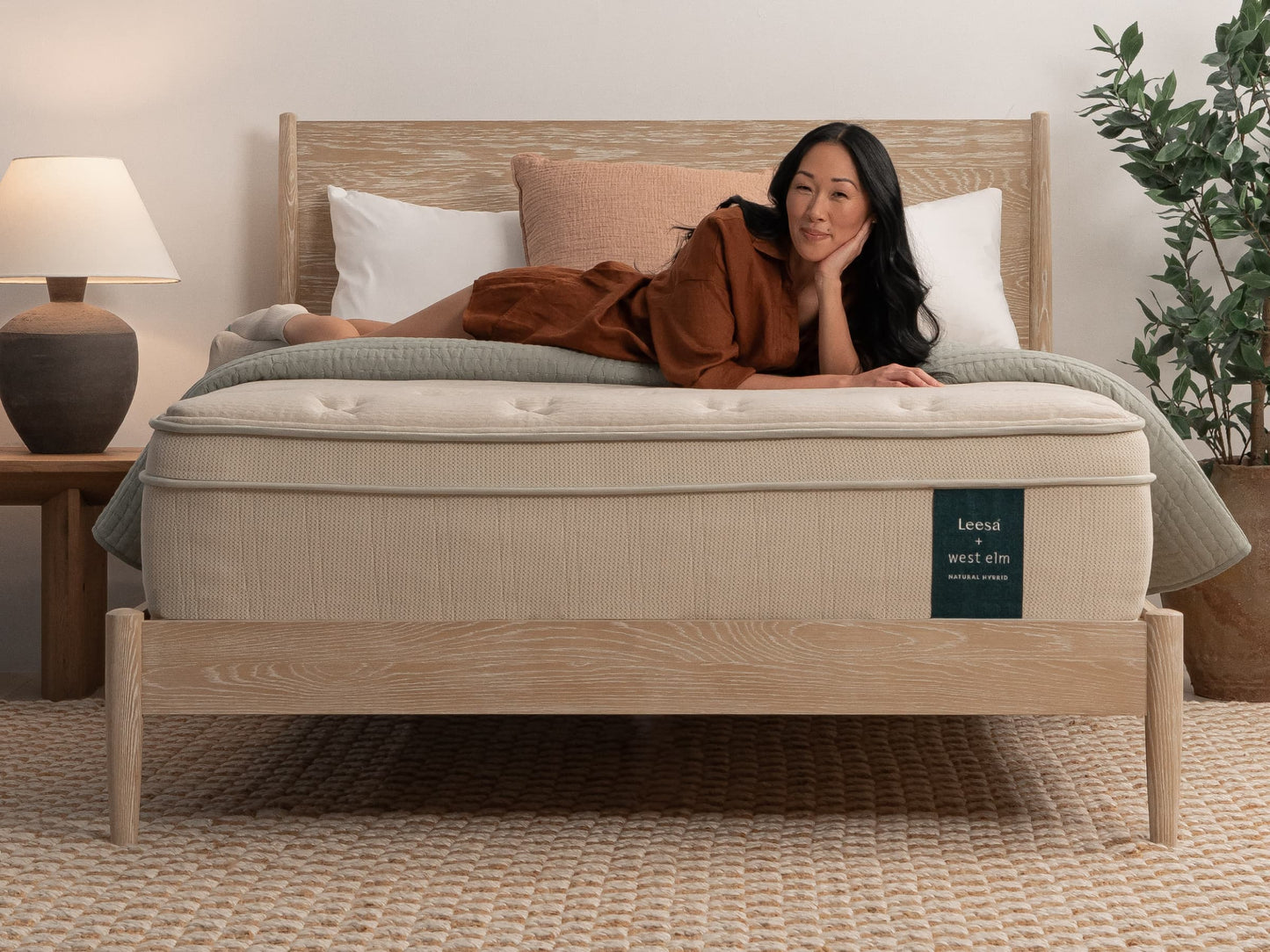Woman lying on Leesa + West Elm Natural Hybrid mattress on oak bed frame with pink and white pillows. for The Mattress Shop, showcasing product image for Leesa Natural Hybrid Mattress on the product page.