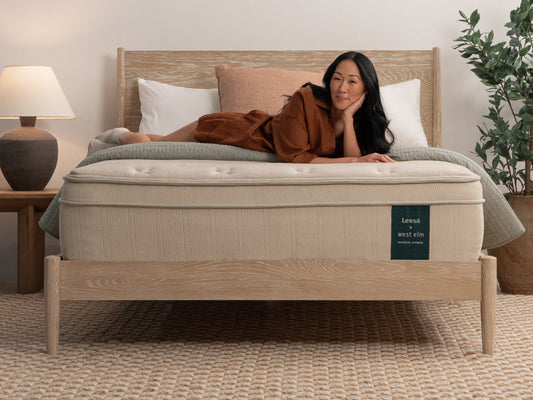 Woman lying on Leesa + West Elm Natural Hybrid mattress on oak bed frame with pink and white pillows. for The Mattress Shop, showcasing product image for Leesa Natural Hybrid Mattress on the collection page.