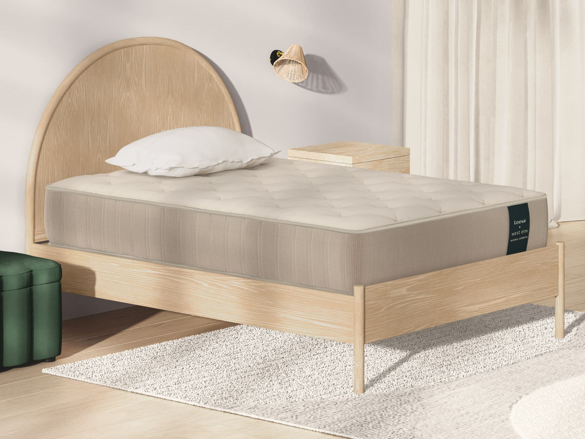 Leesa Natural Essential mattress on an arched oak bed frame in a bedroom with green ottoman and rattan sconce. for The Mattress Shop, showcasing product image for Leesa Natural Essential Hybrid Mattress on the product page.